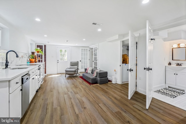 interior space with stainless steel dishwasher, light hardwood / wood-style floors, white cabinetry, and sink