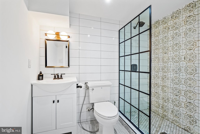 bathroom with toilet, tile patterned floors, vanity, a tile shower, and tile walls