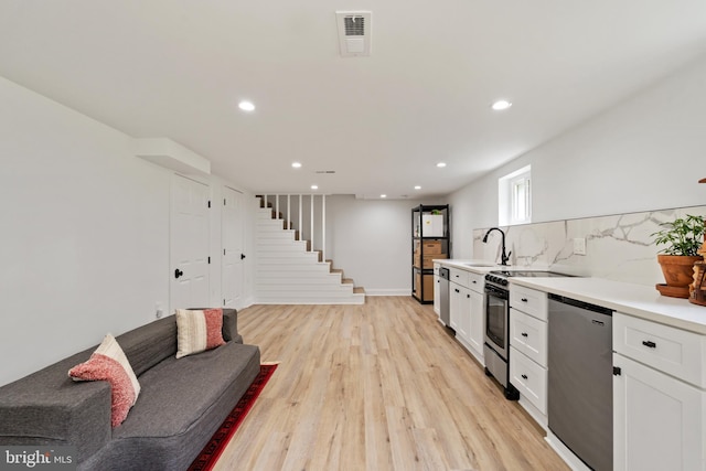 kitchen with backsplash, light hardwood / wood-style flooring, stainless steel appliances, white cabinetry, and sink