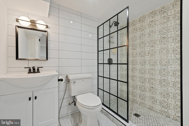 bathroom featuring toilet, tile patterned flooring, vanity, tiled shower, and tile walls