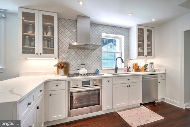 kitchen with light stone counters, stainless steel appliances, sink, wall chimney range hood, and dark hardwood / wood-style floors