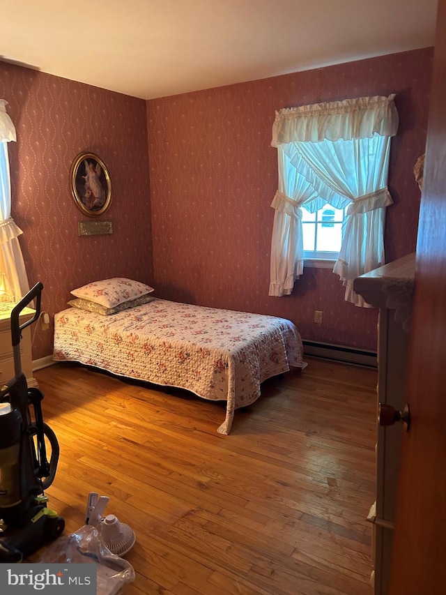 bedroom with a baseboard radiator, wood finished floors, and wallpapered walls