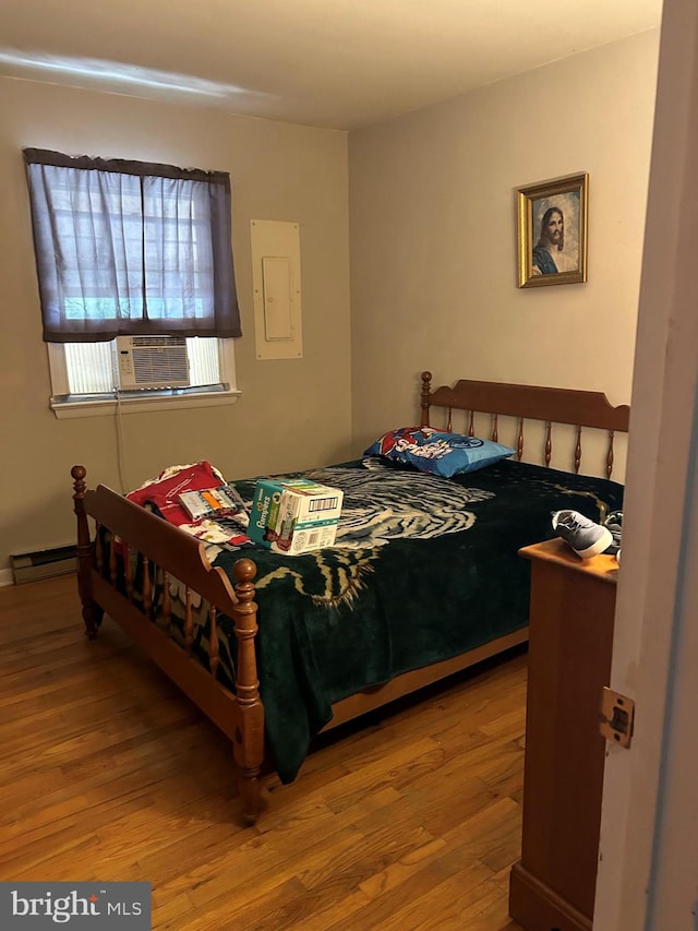 bedroom with electric panel, cooling unit, and wood finished floors