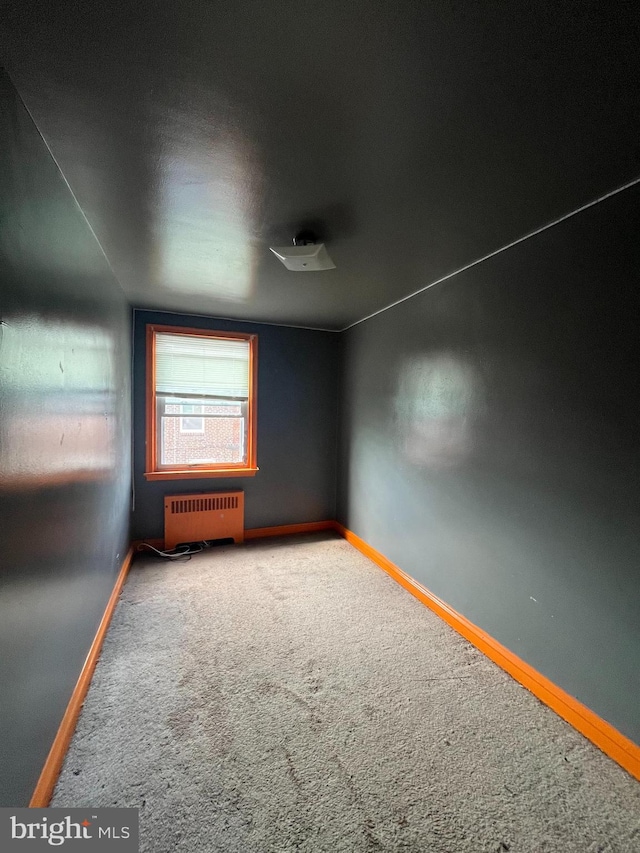 carpeted spare room with radiator and lofted ceiling