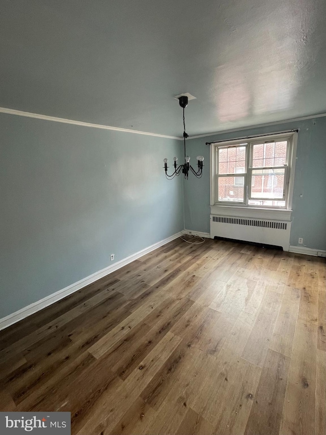 empty room with radiator heating unit, wood-type flooring, and a notable chandelier