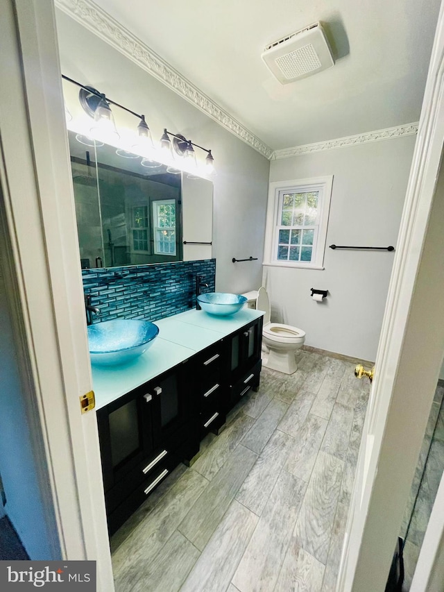 bathroom with toilet, wood-type flooring, backsplash, ornamental molding, and vanity