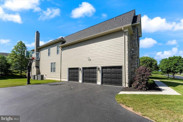 view of side of property with a lawn, cooling unit, and a garage