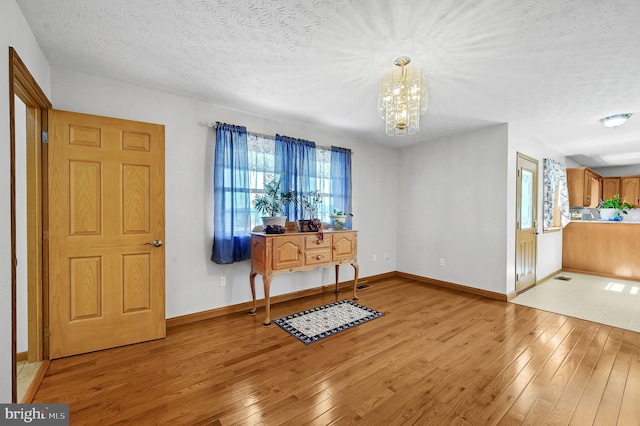 entryway featuring light wood finished floors, a textured ceiling, baseboards, and a notable chandelier