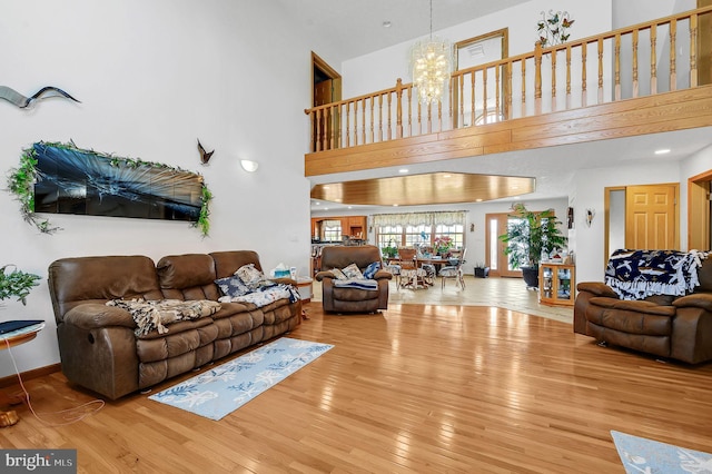 living area featuring baseboards, wood finished floors, a towering ceiling, and an inviting chandelier