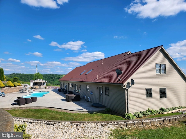 back of property with an outbuilding, an outdoor pool, a patio area, and metal roof