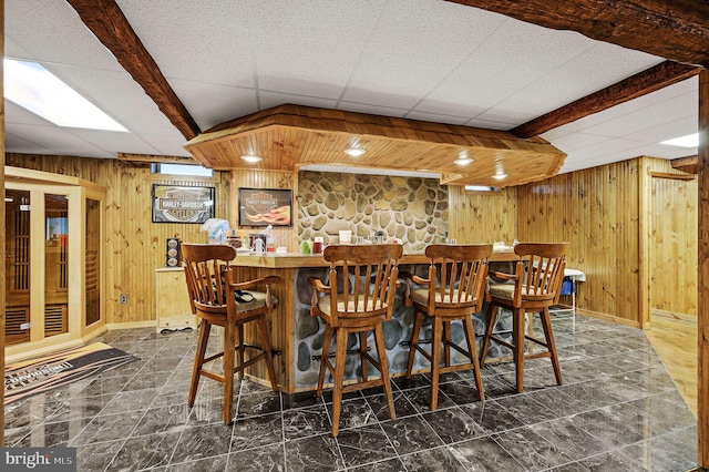 bar with a dry bar, wood walls, baseboards, and a drop ceiling