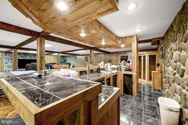 kitchen featuring brown cabinets, tile countertops, a paneled ceiling, wood walls, and a peninsula