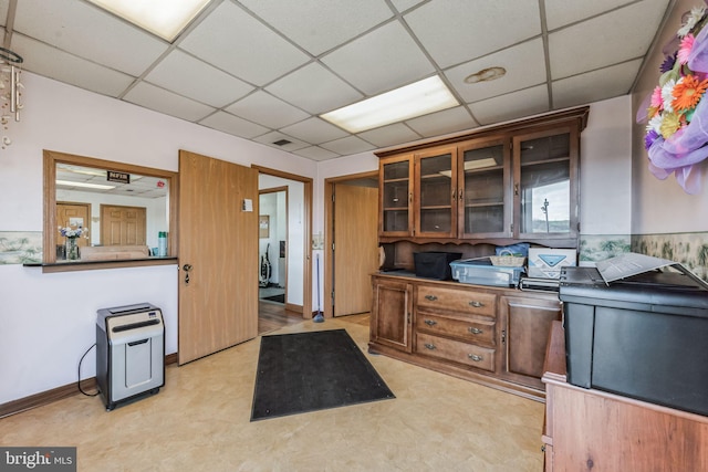 kitchen with light floors, brown cabinetry, a drop ceiling, and glass insert cabinets