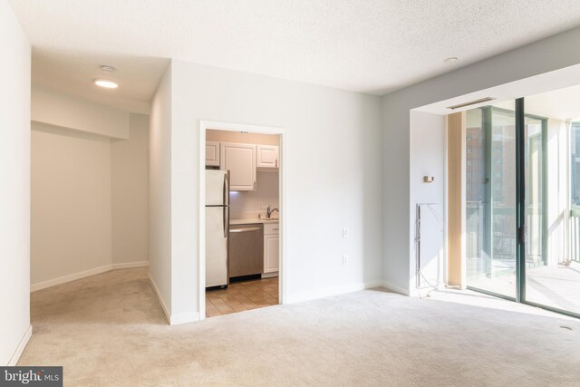 unfurnished bedroom with light carpet, stainless steel refrigerator, a textured ceiling, access to outside, and ensuite bath