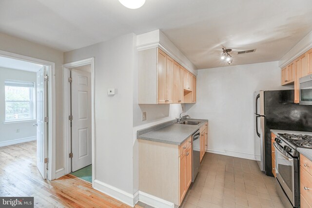 kitchen with light wood-type flooring, stainless steel appliances, light brown cabinetry, sink, and ceiling fan