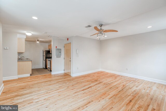 unfurnished living room with electric panel, light hardwood / wood-style flooring, ceiling fan, and sink