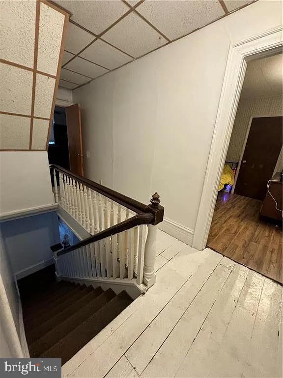 staircase with a paneled ceiling and hardwood / wood-style flooring