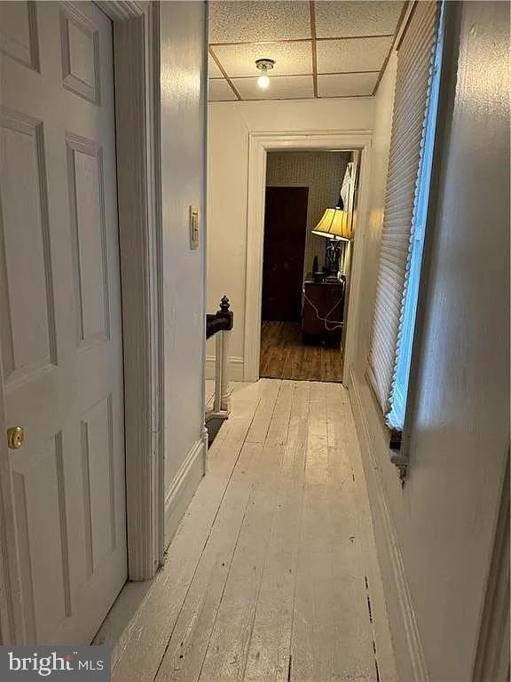 hallway with hardwood / wood-style floors and a paneled ceiling