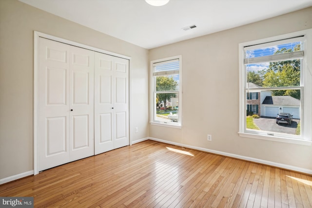 unfurnished bedroom featuring baseboards, wood-type flooring, a closet, and visible vents