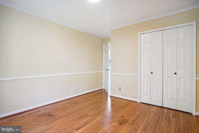 unfurnished bedroom with hardwood / wood-style floors, crown molding, baseboards, and a closet