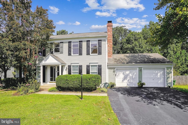 colonial-style house with a front lawn, fence, aphalt driveway, a chimney, and a garage