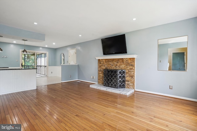 unfurnished living room with hardwood / wood-style flooring, recessed lighting, a fireplace with raised hearth, and baseboards