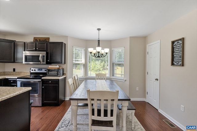 kitchen with pendant lighting, stainless steel appliances, light stone counters, an inviting chandelier, and dark wood-type flooring