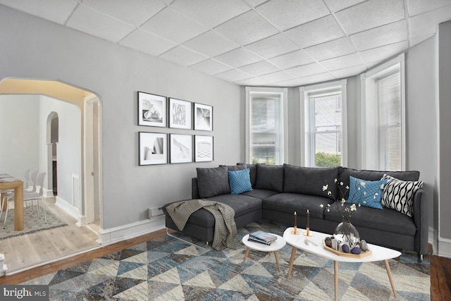 living area featuring a paneled ceiling, arched walkways, baseboards, and wood finished floors