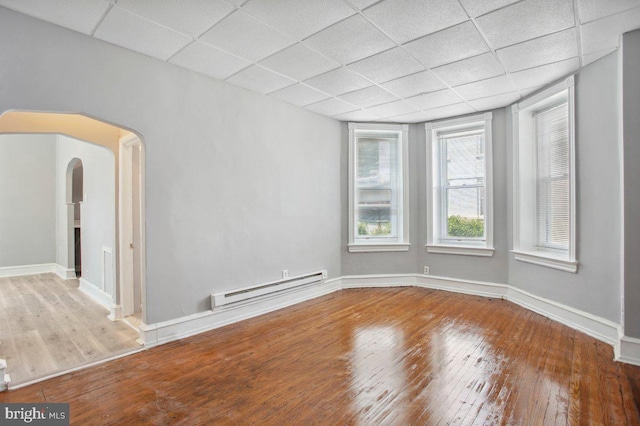 empty room featuring baseboard heating, wood-type flooring, and a paneled ceiling