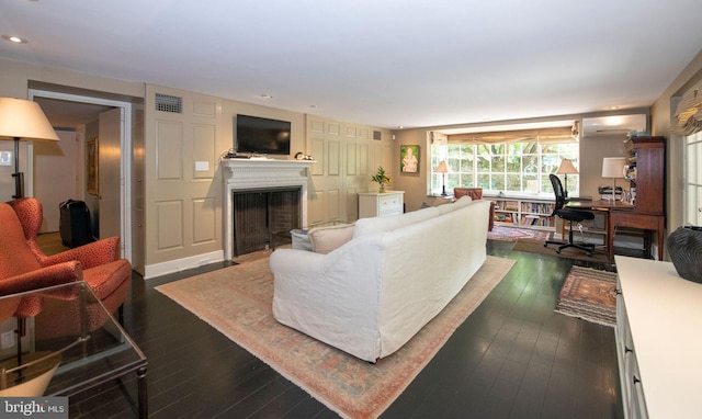 living room with dark wood-style flooring, a wall mounted air conditioner, a fireplace, and visible vents