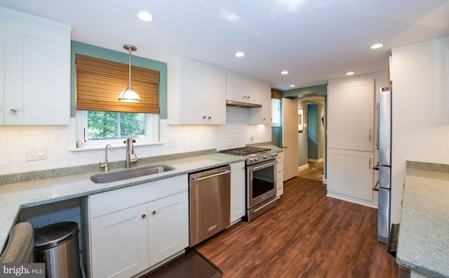 kitchen featuring decorative light fixtures, dark wood finished floors, appliances with stainless steel finishes, white cabinets, and a sink