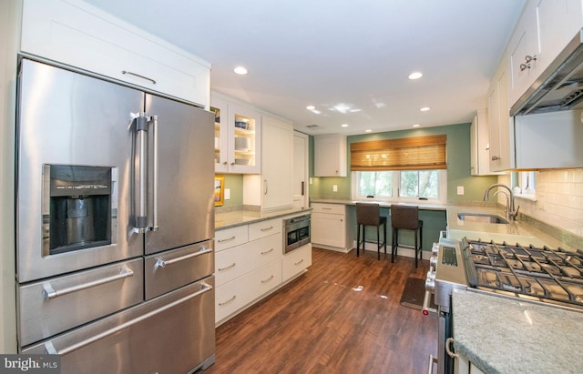 kitchen with dark wood-style flooring, stainless steel appliances, under cabinet range hood, white cabinetry, and a sink