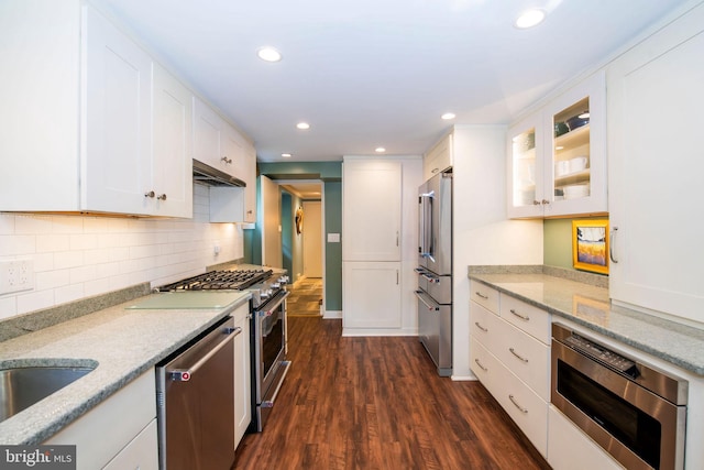 kitchen with decorative backsplash, appliances with stainless steel finishes, dark wood-type flooring, white cabinets, and light stone countertops