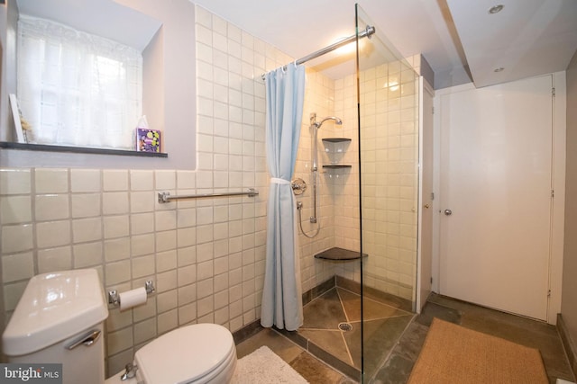 full bathroom featuring toilet, a tile shower, and tile walls