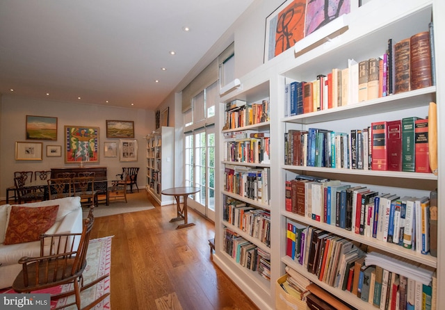 living area featuring wall of books, wood finished floors, and recessed lighting