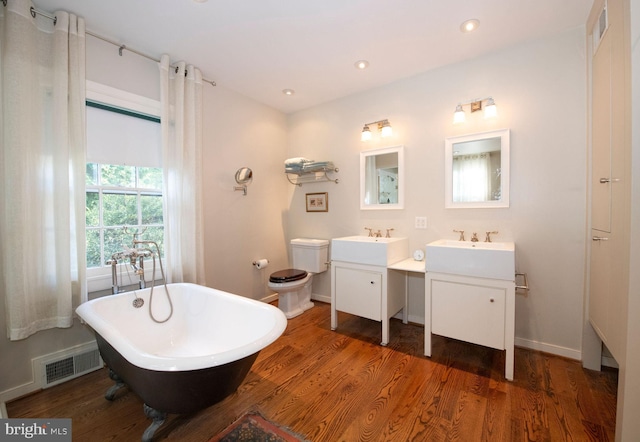 full bath featuring baseboards, visible vents, wood finished floors, a freestanding tub, and two vanities