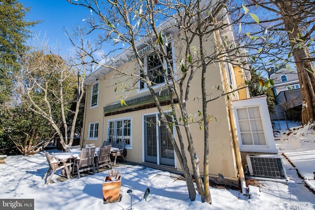 snow covered back of property featuring a patio, outdoor dining area, central AC, and stucco siding