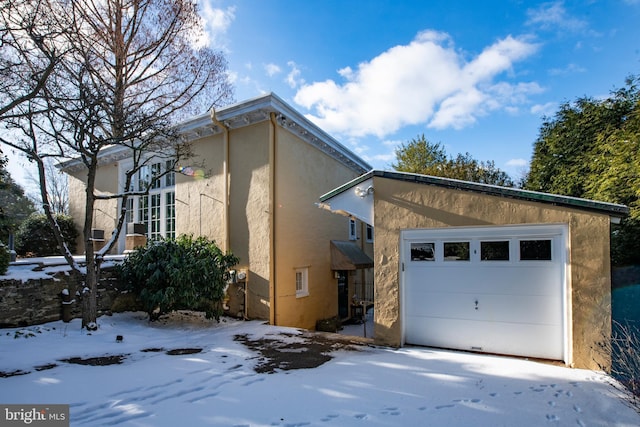 snow covered property featuring an attached garage and stucco siding