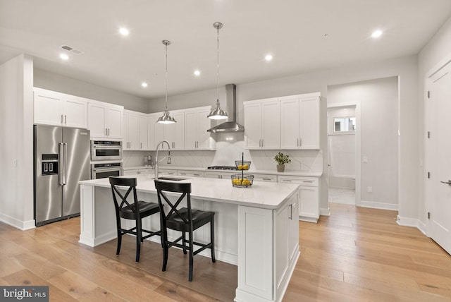 kitchen featuring a center island with sink, light hardwood / wood-style flooring, stainless steel appliances, and wall chimney range hood