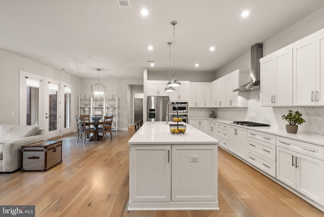 kitchen featuring white cabinets, a center island, stainless steel appliances, light hardwood / wood-style floors, and wall chimney exhaust hood