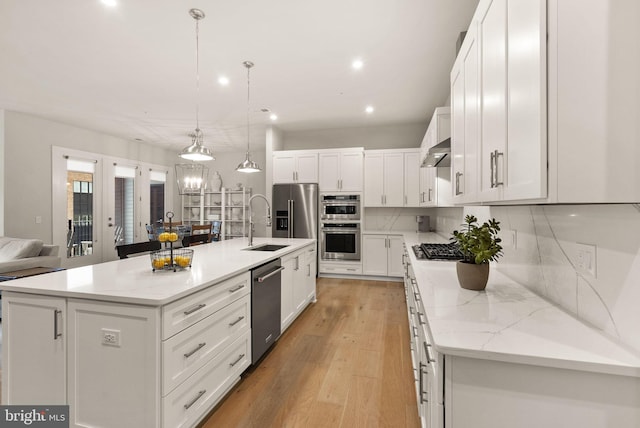 kitchen featuring range hood, french doors, appliances with stainless steel finishes, a center island with sink, and light hardwood / wood-style floors