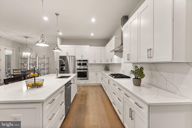 kitchen featuring a kitchen island with sink, light wood-type flooring, stainless steel appliances, light stone counters, and sink