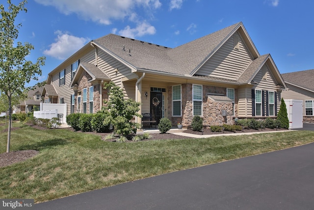 view of front of property with a shingled roof, a front yard, stone siding, and fence