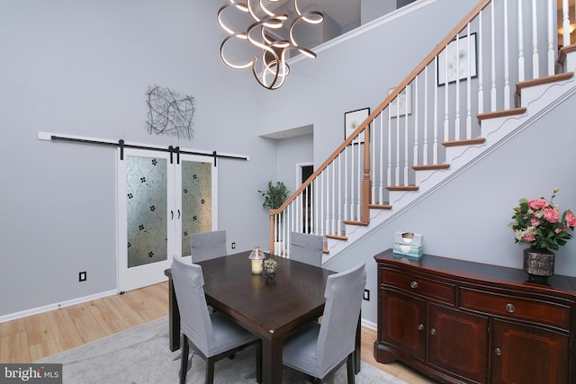 dining room with light wood-type flooring, a barn door, a chandelier, and a high ceiling