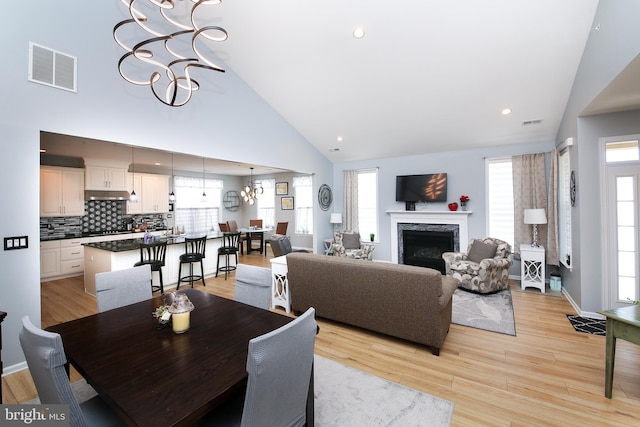 dining area featuring a premium fireplace, a notable chandelier, light hardwood / wood-style flooring, and high vaulted ceiling