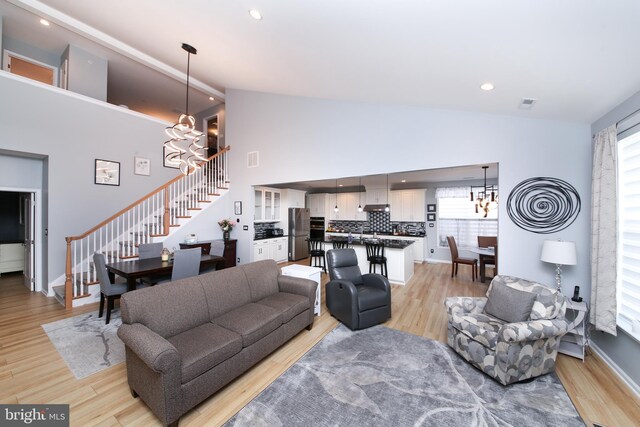 living room featuring light wood-type flooring, high vaulted ceiling, and a chandelier