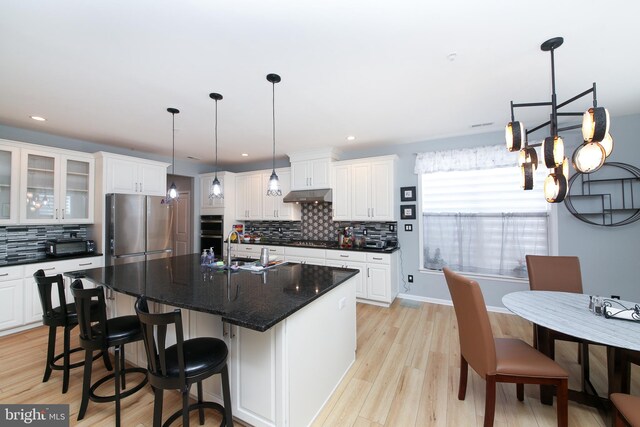 kitchen featuring a kitchen island with sink, tasteful backsplash, stainless steel appliances, and white cabinets