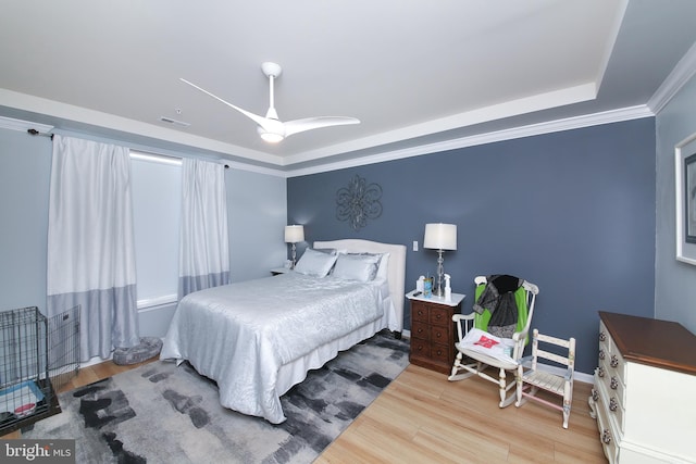 bedroom with crown molding, ceiling fan, light wood-type flooring, and a tray ceiling