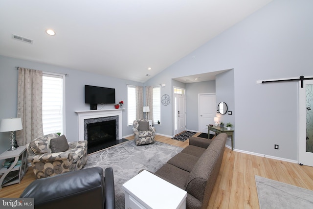 living room featuring light hardwood / wood-style flooring, a barn door, high vaulted ceiling, and a premium fireplace