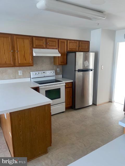 kitchen featuring stainless steel fridge, white electric range oven, kitchen peninsula, and tasteful backsplash